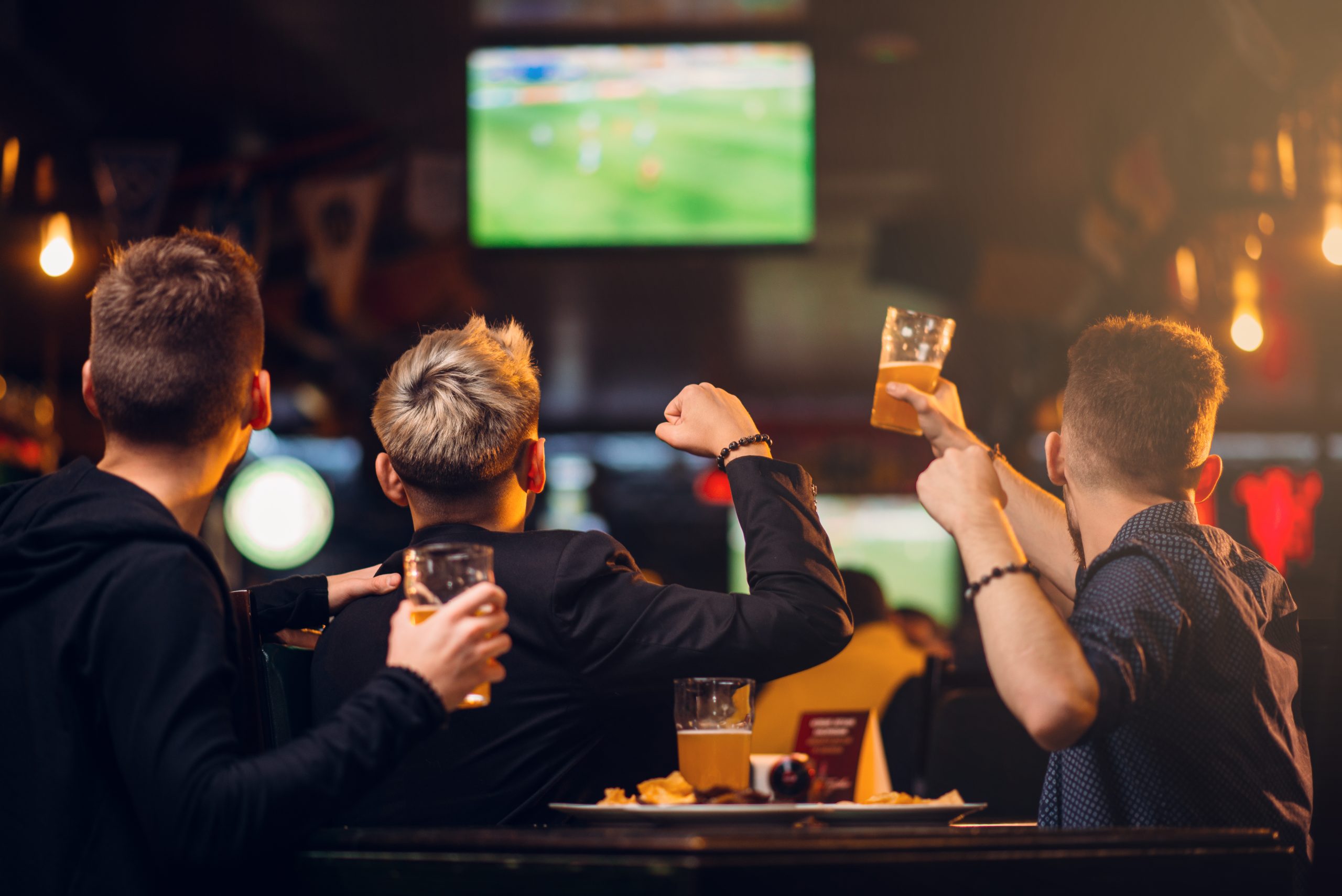 Three men watches football on TV in a sport bar, happy leisure of fan company